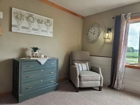 A room with a dresser, a chair, a wall clock, and a window with curtains.