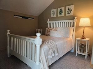 A bedroom with a white bed, a bedside table with a lamp, and wall art.