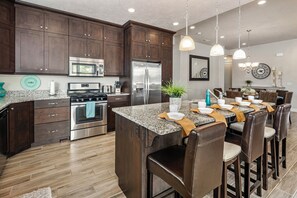 A modern kitchen with dark wood cabinets, stainless steel appliances, and a central island with bar stools. - PV 8: Private Spa, BBQ, Air Hockey & Resort Amenities (Santa Clara)