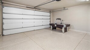 En garage med en lukket hvid garageport, en loftventilator og et billardbord.