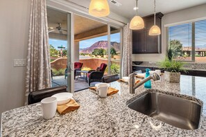 A kitchen with granite countertops, a stainless steel sink, and a view of a mountainous landscape through large sliding glass doors. - PV 8: Private Spa, BBQ, Air Hockey & Resort Amenities (Santa Clara)