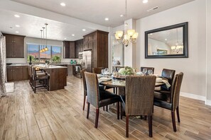 A modern kitchen with dark wood cabinets, a central island, and a dining area with wicker chairs and a chandelier. - PV 8: Private Spa, BBQ, Air Hockey & Resort Amenities (Santa Clara)
