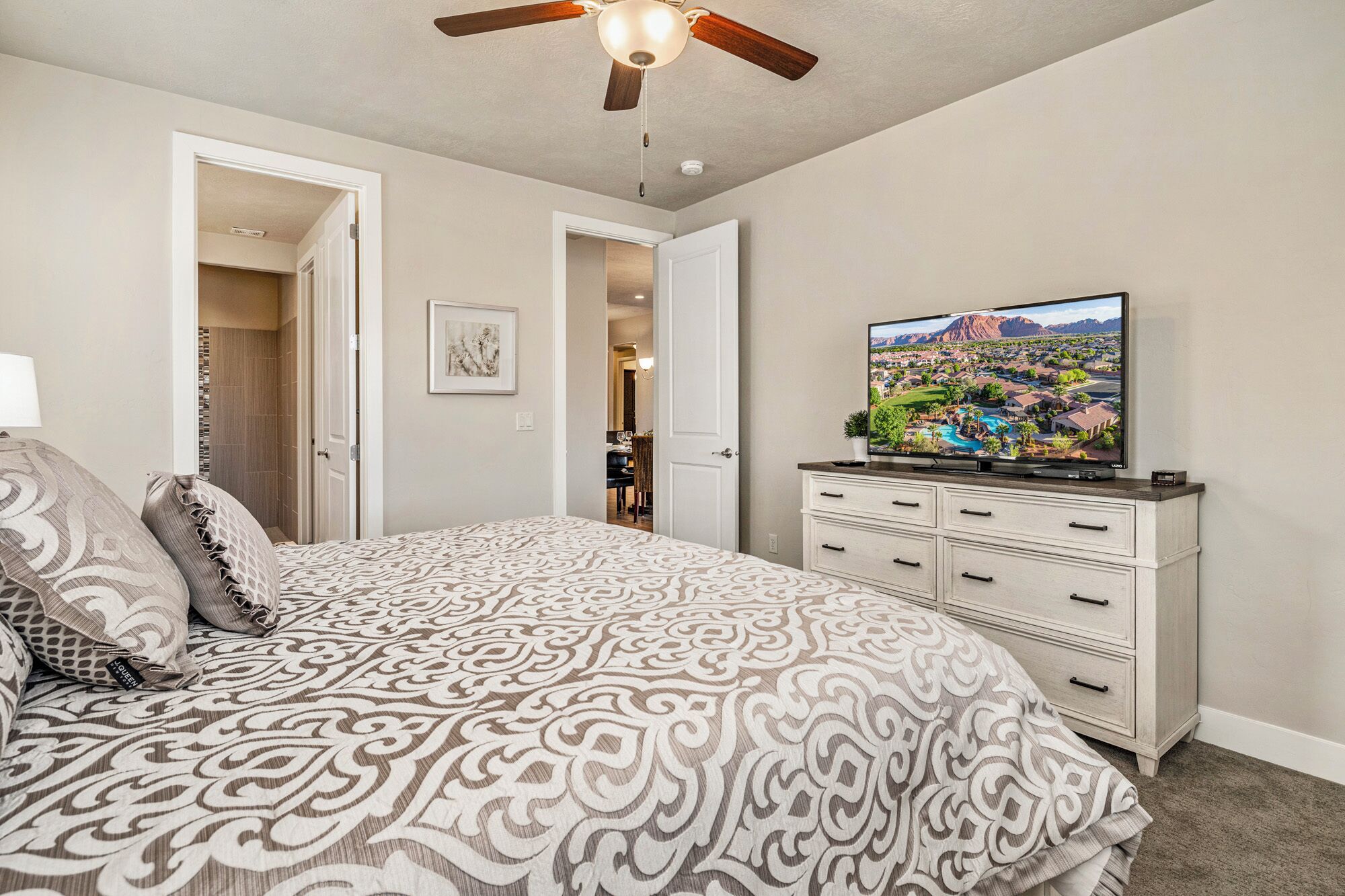 Ein Schlafzimmer mit einem Bett, einem Fernseher auf einer Kommode und einem Deckenventilator.