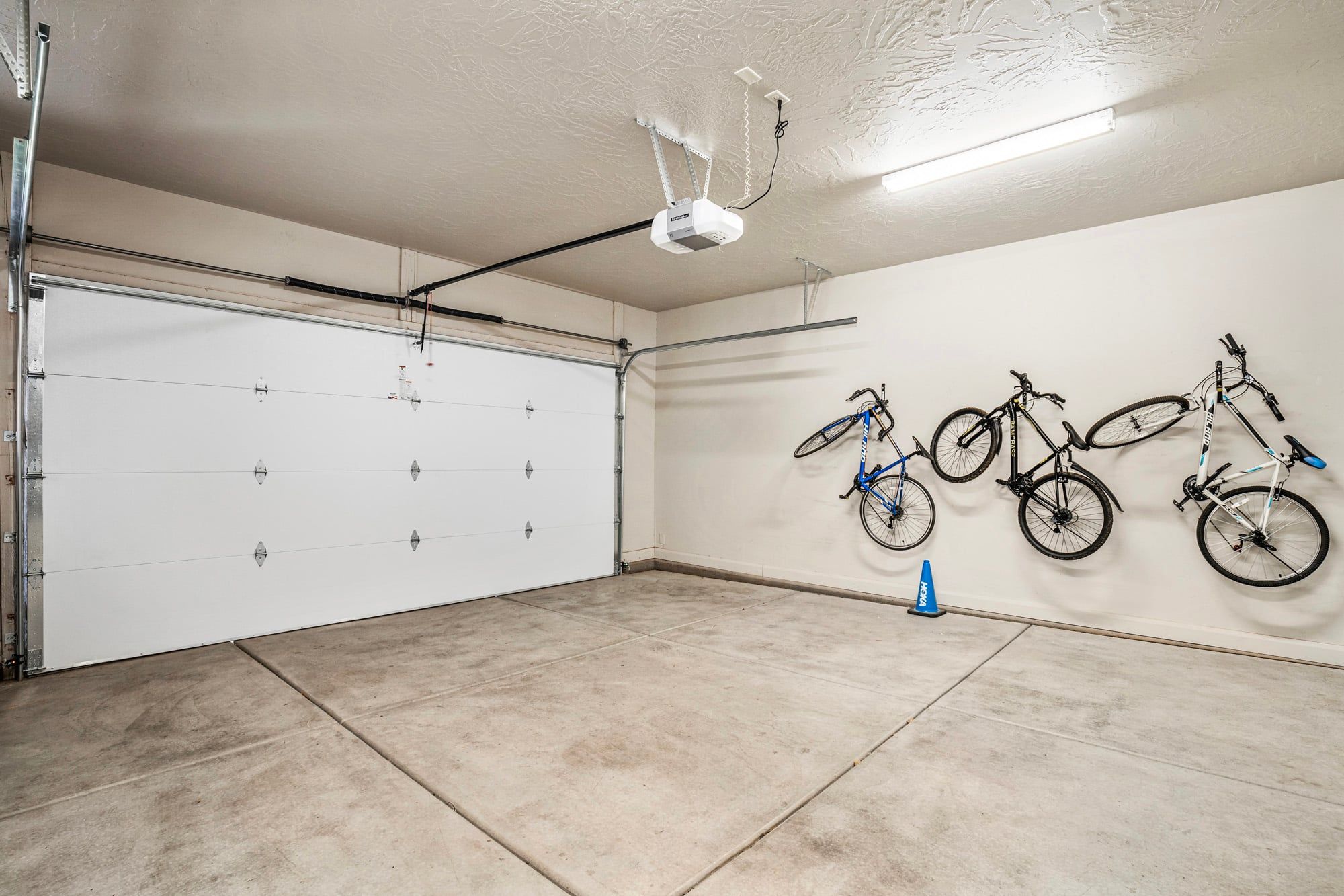 Een garage met een witte garagedeur, een projector in het plafond en drie fietsen aan de muur.