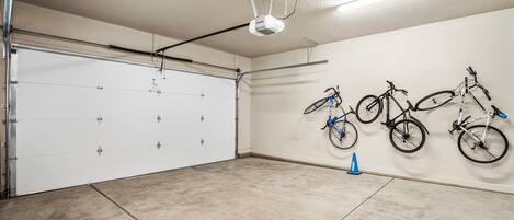Een garage met een witte garagedeur, een projector in het plafond en drie fietsen aan de muur.