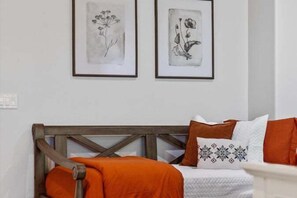 Ein Bett mit Holz-Kopfstück, orangefarbener Bettwäsche und zwei gerahmten Pflanzenbildern an der Wand.