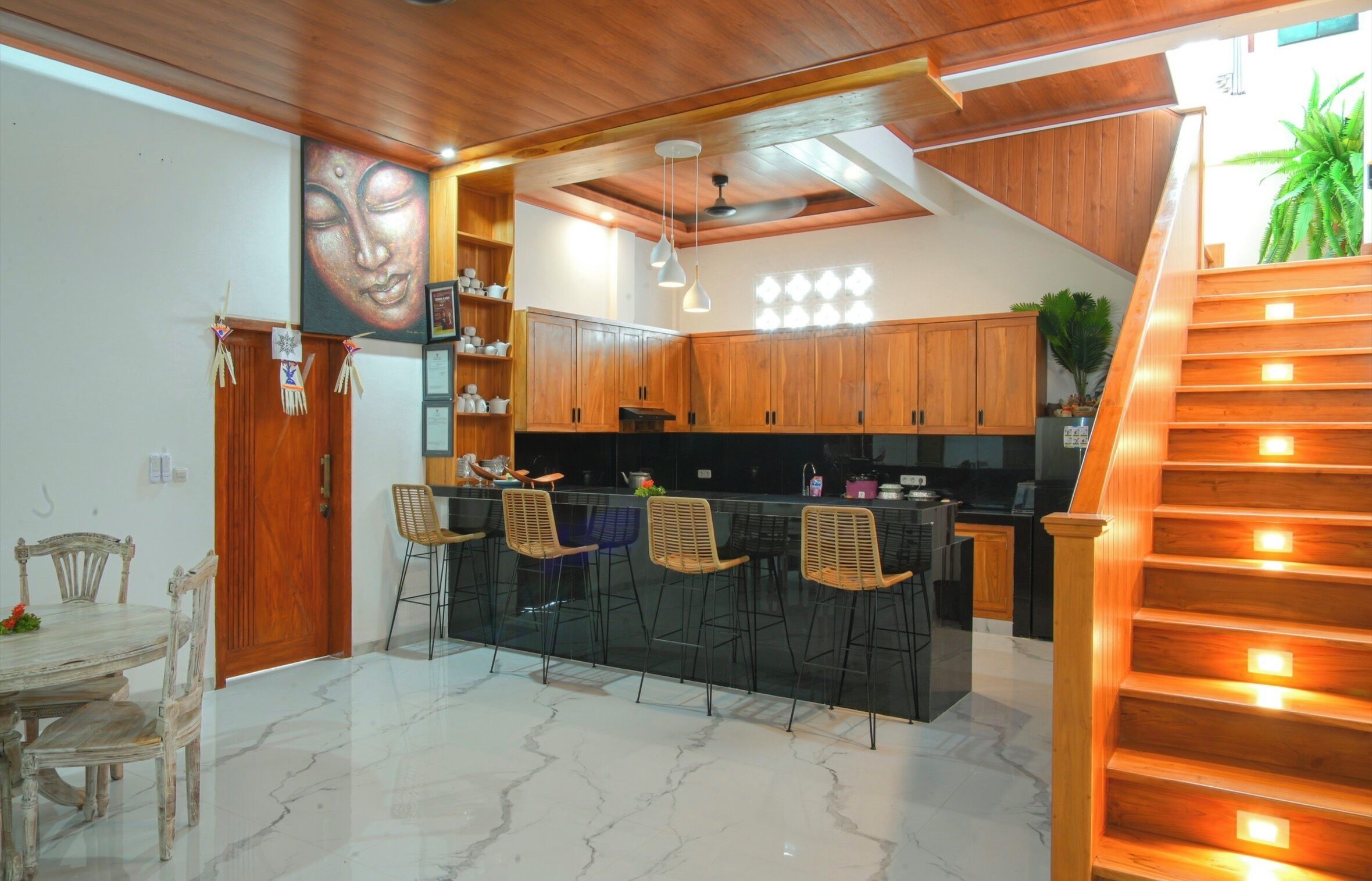 A modern kitchen with wooden cabinets, a central island with bar stools, and a staircase with illuminated steps.