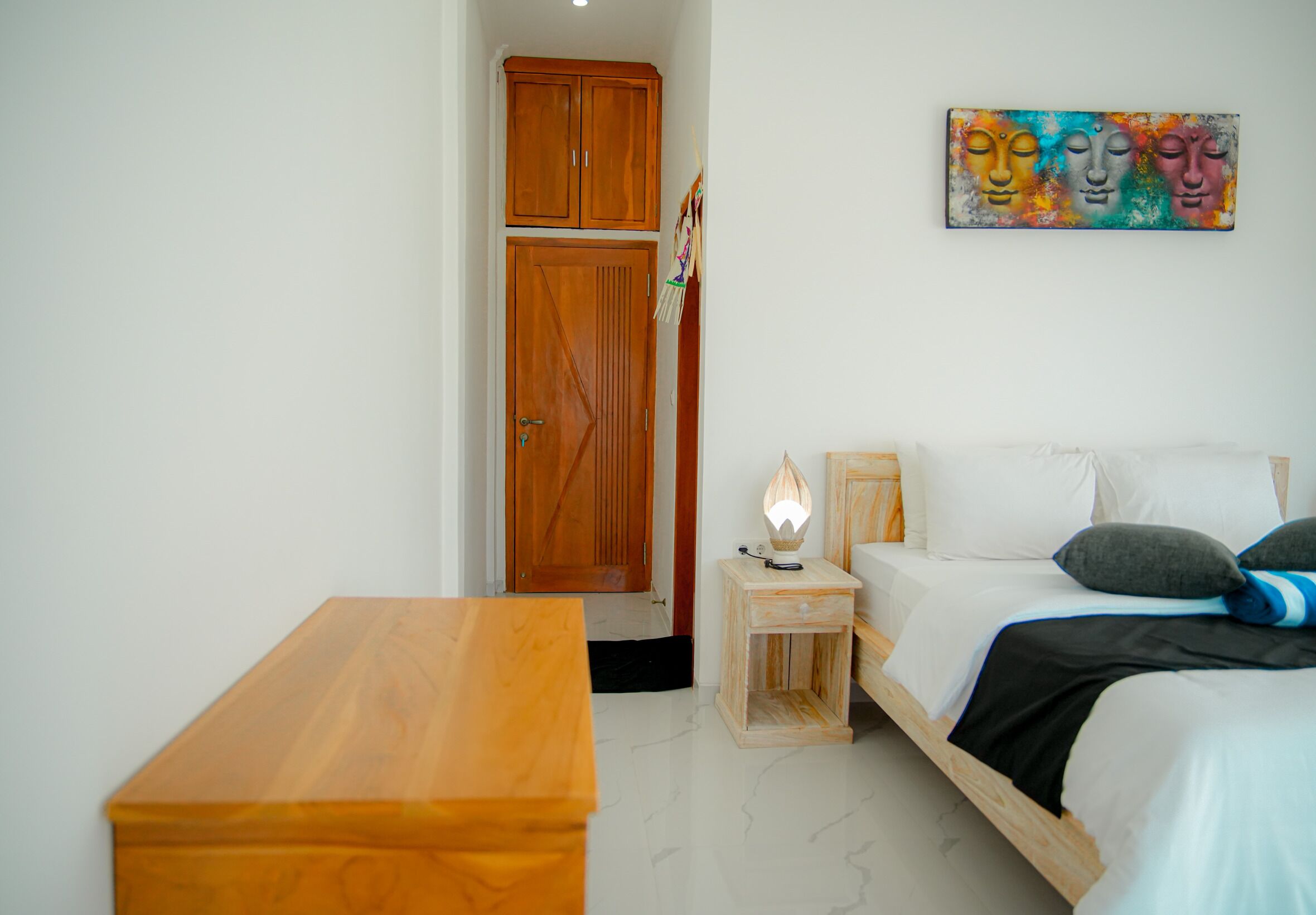 Ein Schlafzimmer mit einem Holzbett, einem Nachttisch mit Lampe, einer Holzbank, einem Kleiderschrank und einem farbenfrohen Bild an der Wand.