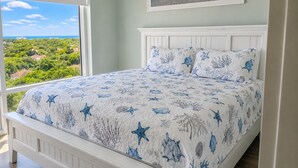 A bedroom with a large window, a bed with a starfish and coral pattern bedspread, and a framed picture of a beach scene on the wall. - 10th-Floor Luau Condo | Fabulous South-Facing Gulf Views & Beach Access (Miramar Beach)
