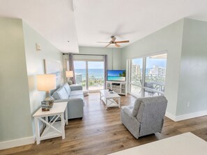 A modern living room with a flat-screen TV, a ceiling fan, and a view of the ocean. - 10th-Floor Luau Condo | Fabulous South-Facing Gulf Views & Beach Access (Miramar Beach)