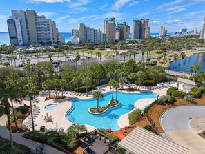 A resort with a large pool, palm trees, and a view of the ocean and city skyline. - 10th-Floor Luau Condo | Fabulous South-Facing Gulf Views & Beach Access (Miramar Beach)