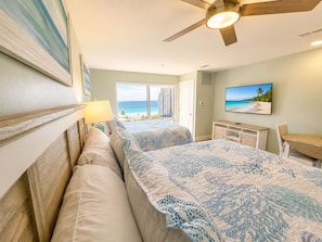 A bedroom with a bed, a desk, a chair, a ceiling fan, and a TV. - NEW !!! Luau 2–7034 | 10th-Floor Studio, 2 Queens,  south facing Gulf Views, Pool & Beach Tram (Miramar Beach)
