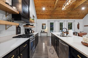 A modern kitchen with black cabinets, a stainless steel range, and a wooden ceiling. - Private & Romantic | Hot Tub, ATV Trails access (Broken Bow)