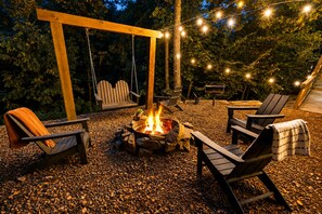 Ein Außenbereich mit Adirondack-Stühlen, einem Feuerkorb und Lichterketten.