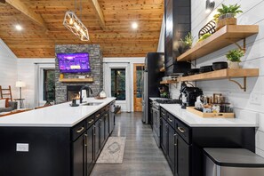 A modern kitchen with a central island, black cabinetry, and a stone accent wall. - Private & Romantic | Hot Tub, ATV Trails access (Broken Bow)