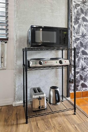 A kitchen area with a microwave, toaster, and kettle on a metal rack. - Steps to Waikiki Beach | Prime Beach Location! (Honolulu)