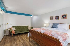 A bedroom with a wooden bed, a green sofa, a small side table, and a lamp. - Steps to Waikiki Beach | Surf~Hike~Dine (Honolulu)
