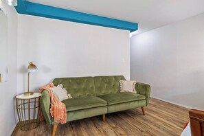 A green sofa with a cushion, a small round table with a lamp, and a wooden floor. - Steps to Waikiki Beach | Prime Beach Location! (Honolulu)