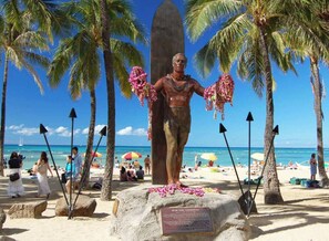 Ein Strand mit einer Statue, Palmen und Menschen.