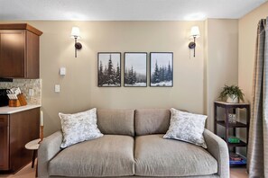 A living room with a beige sofa, two wall-mounted lamps, and three framed pictures depicting snowy forests.
