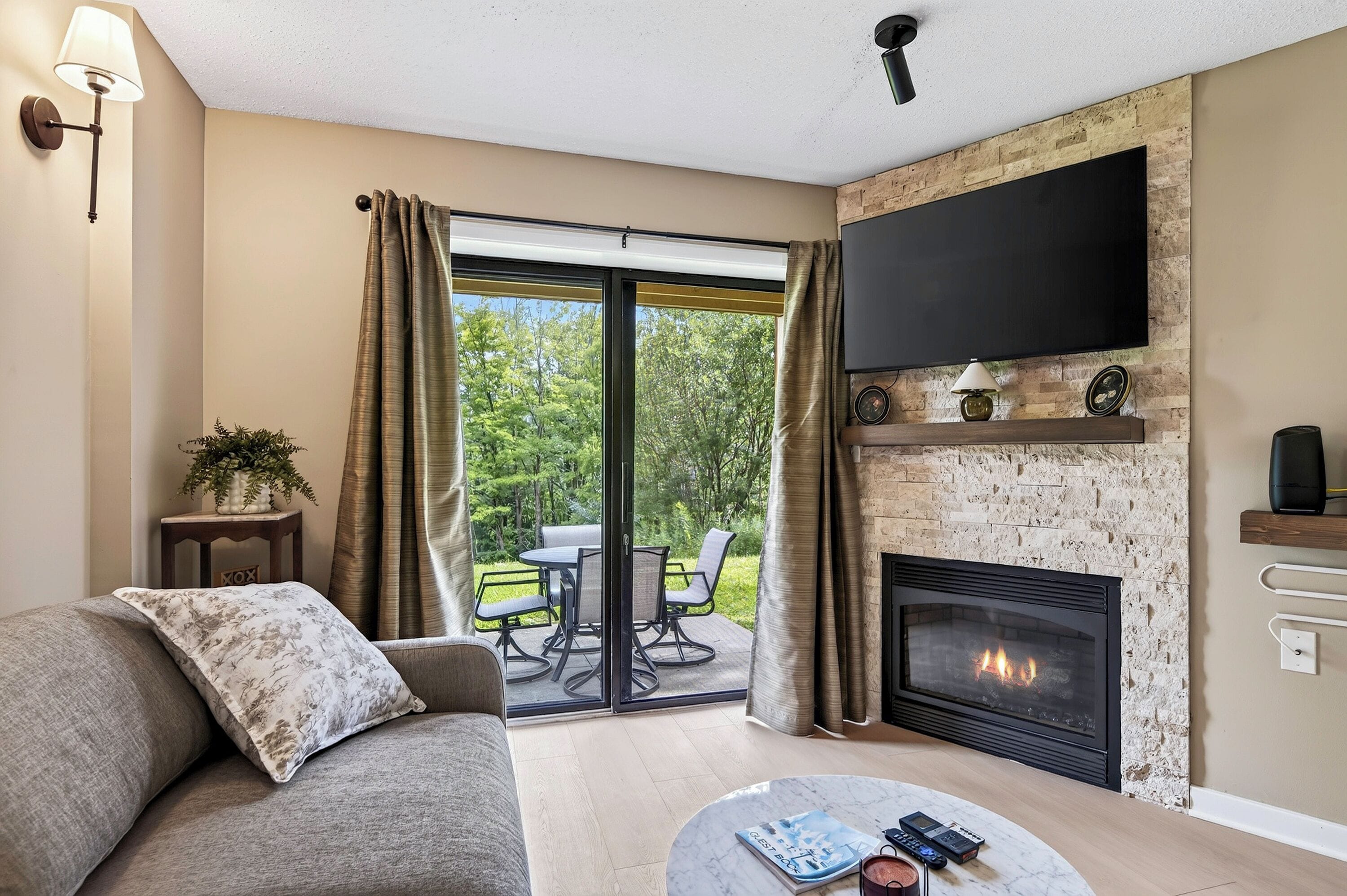 A living room with a fireplace, a sofa, a coffee table with books and remotes, and a TV mounted on the wall.