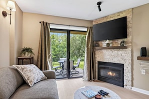 A living room with a fireplace, a sofa, a coffee table with books and remotes, and a TV mounted on the wall.