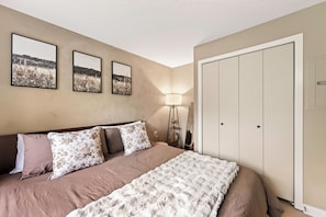 A bedroom with a bed, a nightstand, a lamp, and a wardrobe. - Ski In/Out Condo with King Bed, Fireplace & Patio (Great Valley)
