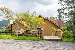 A wooden building with a ramp leading to a wooden deck, surrounded by greenery and a gravel path. - Ski In/Out Condo with King Bed, Fireplace & Patio (Great Valley)