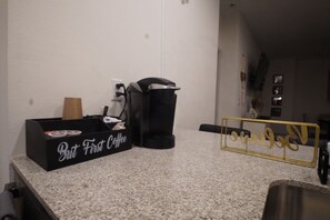 A kitchen counter with a coffee maker, a box labeled 'But First Coffee,' and a gold-framed sign with the word 'love.' - Cozy 1-bedroom apartment in gorgeous The Woodlands with AC (The Woodlands)