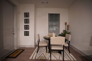 A dining area with a table set for two, chairs, a window with blinds, and decorative wall art. - Cozy 1-bedroom apartment in gorgeous The Woodlands with AC (The Woodlands)