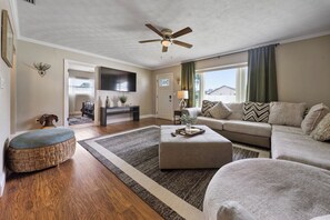Ein Wohnzimmer mit Deckenventilator, Flachbildfernseher, einer Couch, einem Couchtisch und Holzboden.