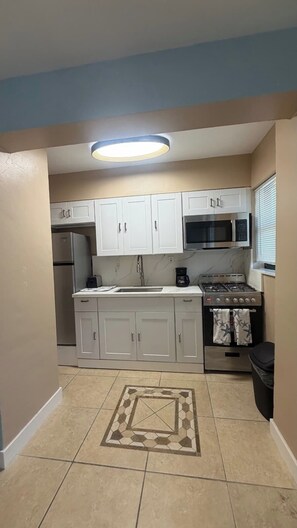 A kitchen with white cabinets, a microwave, a stove, and a tiled floor. - Free Parking Ocean Studio Full Kitchen (Hollywood)