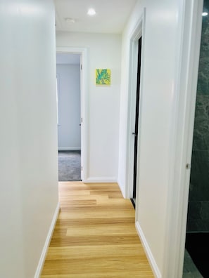 A hallway with a wooden floor, white walls, and a door leading to another room.