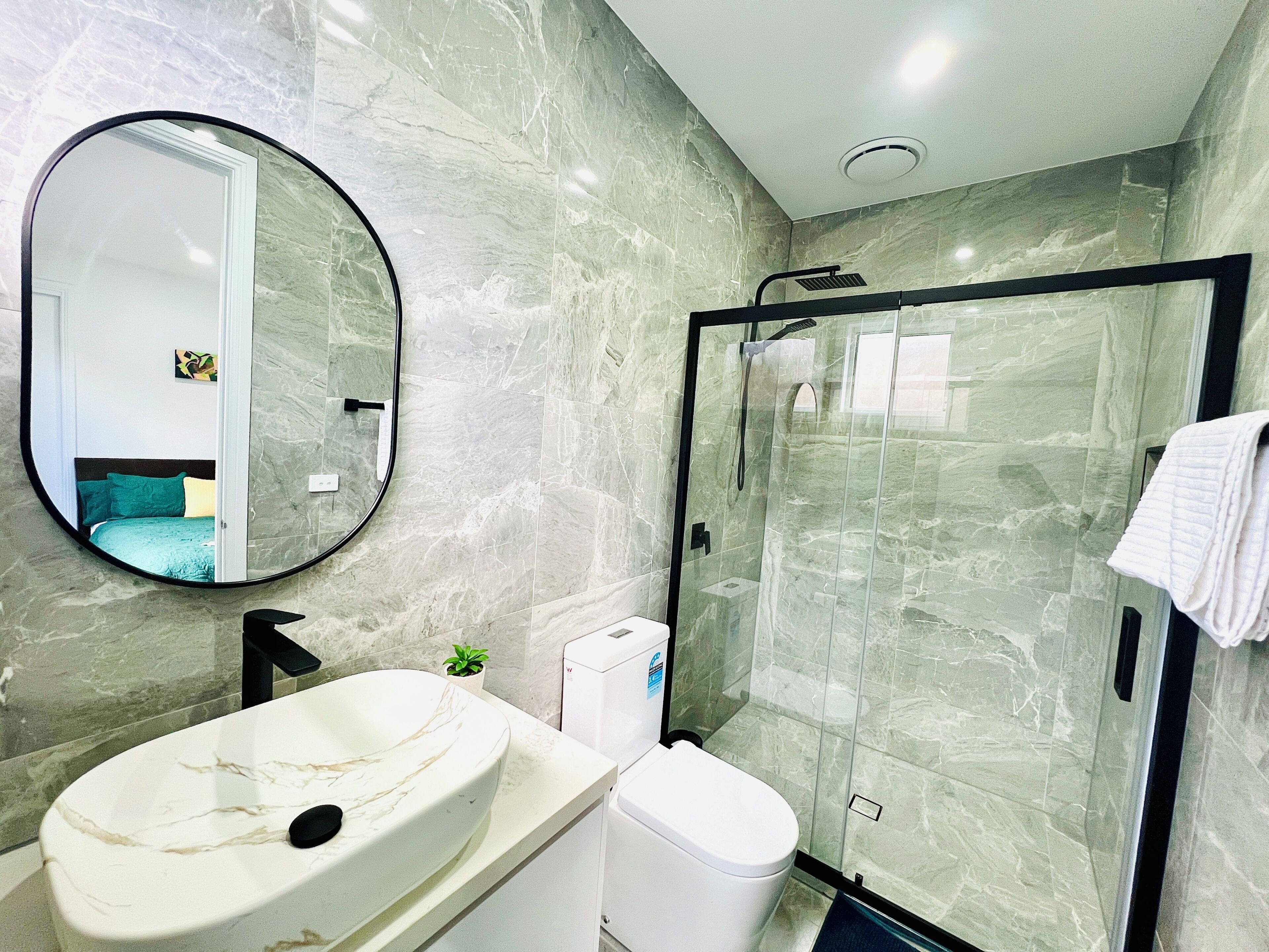 A bathroom with a marble sink, a toilet, a glass shower enclosure, and a mirror.