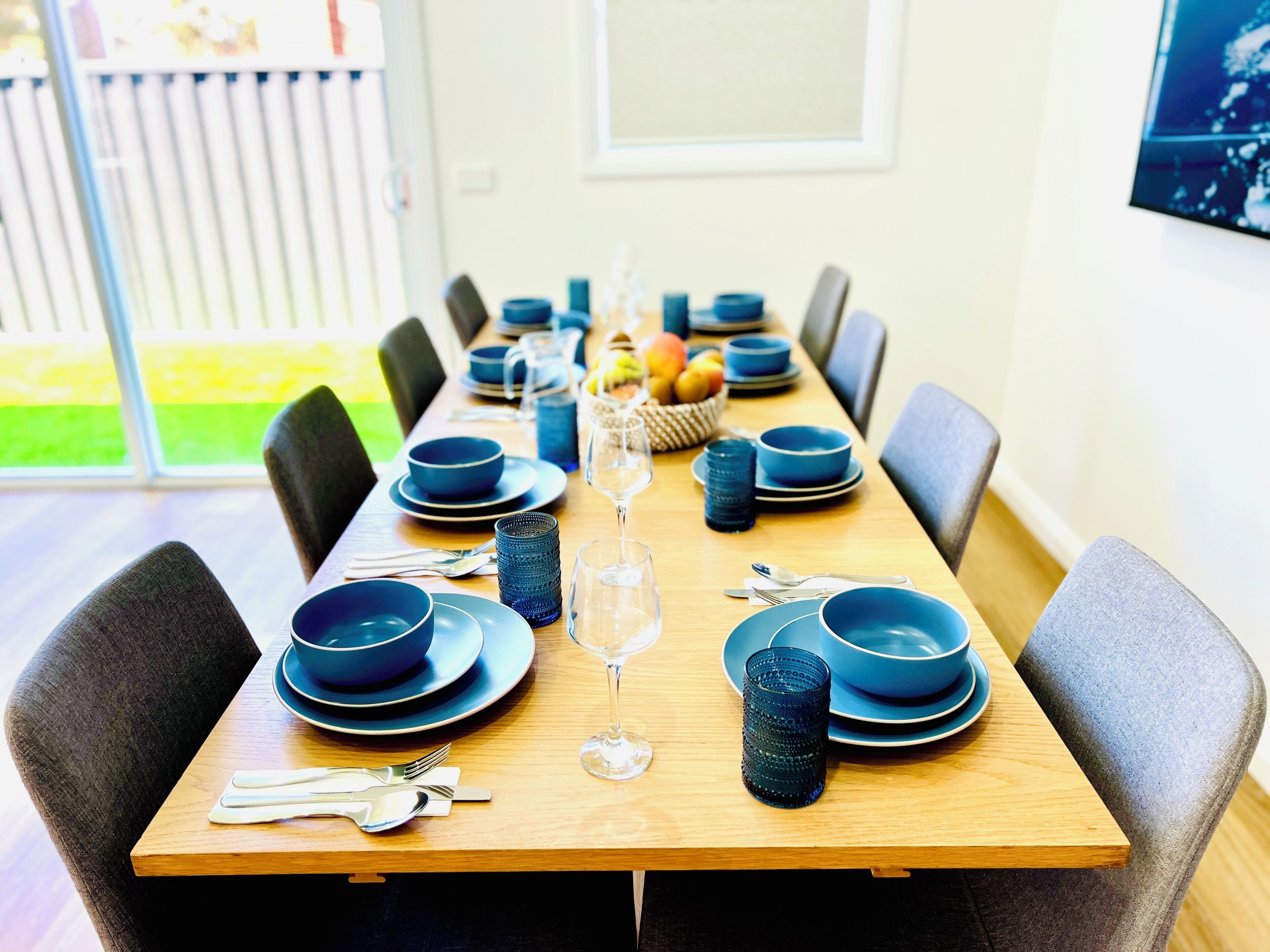 A dining table set with blue plates, glasses, and cutlery, surrounded by chairs.