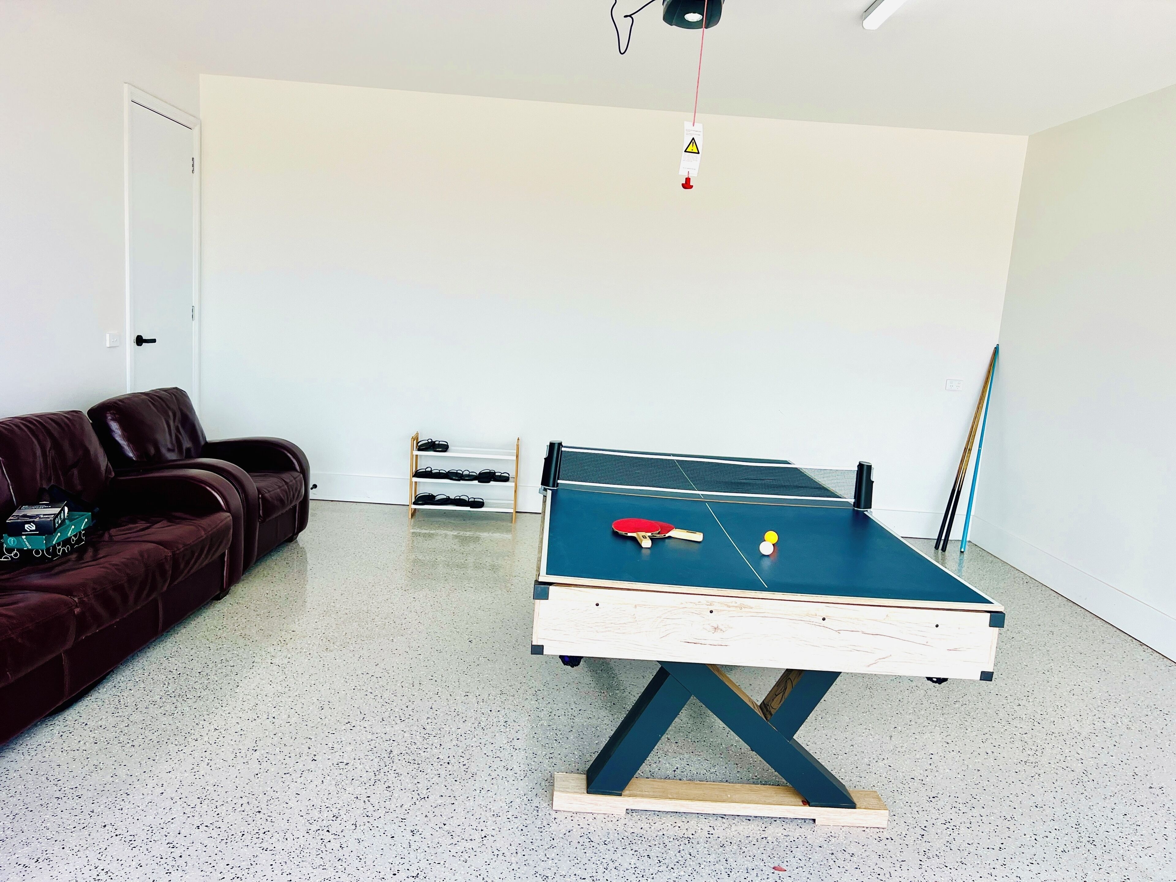 A room with a ping pong table, a sofa, a shoe rack, and a door.