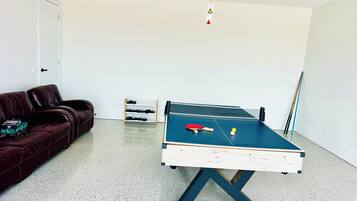 A room with a ping pong table, a sofa, a shoe rack, and a door.