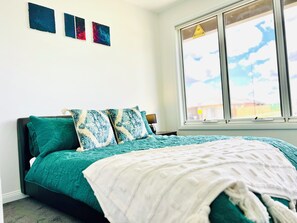 A bedroom with a bed, a window, and three wall art pieces.