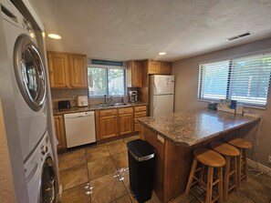 A kitchen with wooden cabinets, a built-in dishwasher, a refrigerator, a coffee maker, and a window with blinds. - En-Tice-ing 1 Bd Getaway Sandy Ut Mtns Ski & I-15 (Sandy)