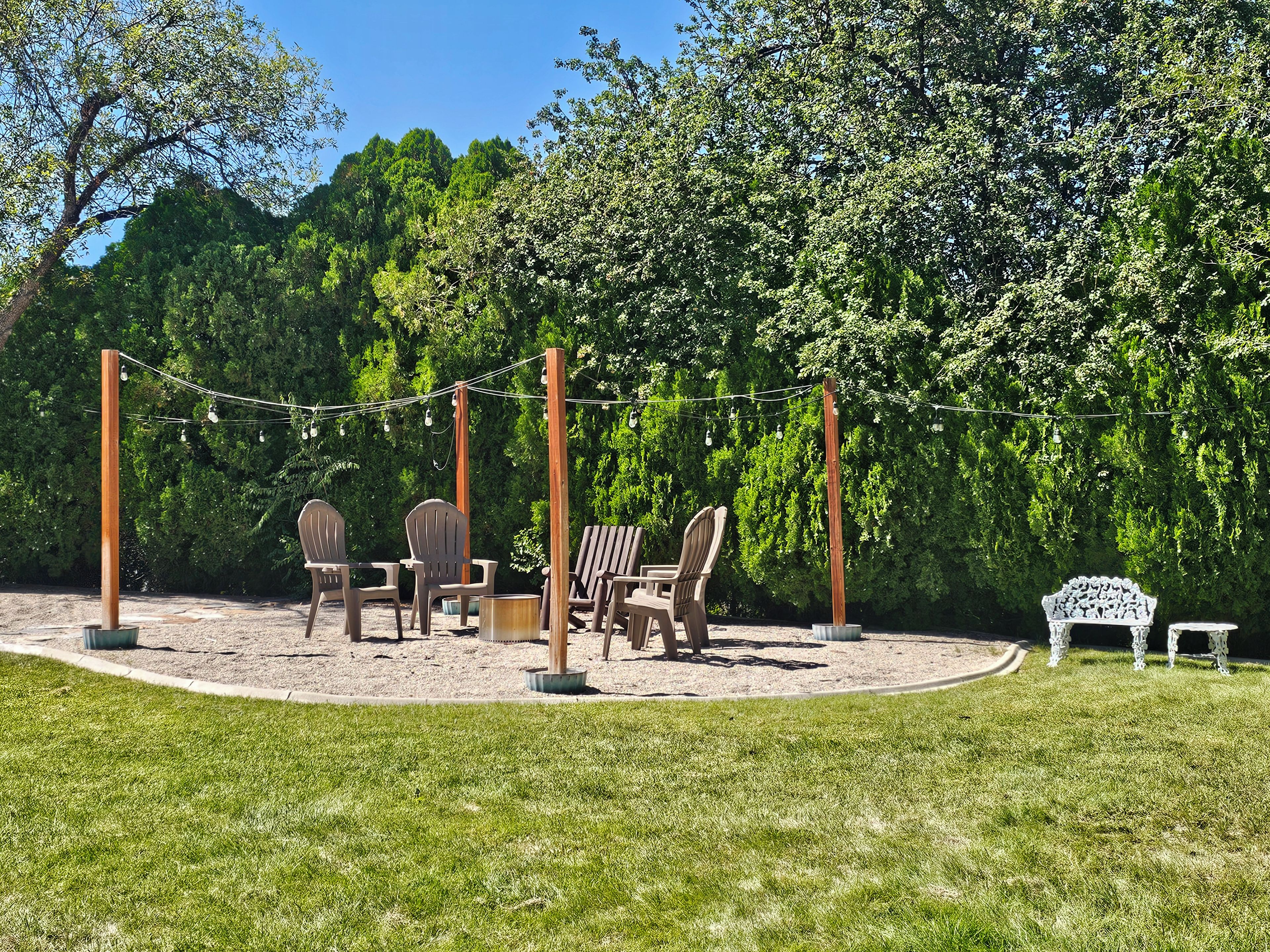 Une aire de jeux avec des chaises en bois et un banc, entourée d’une pelouse et de nombreux arbres.