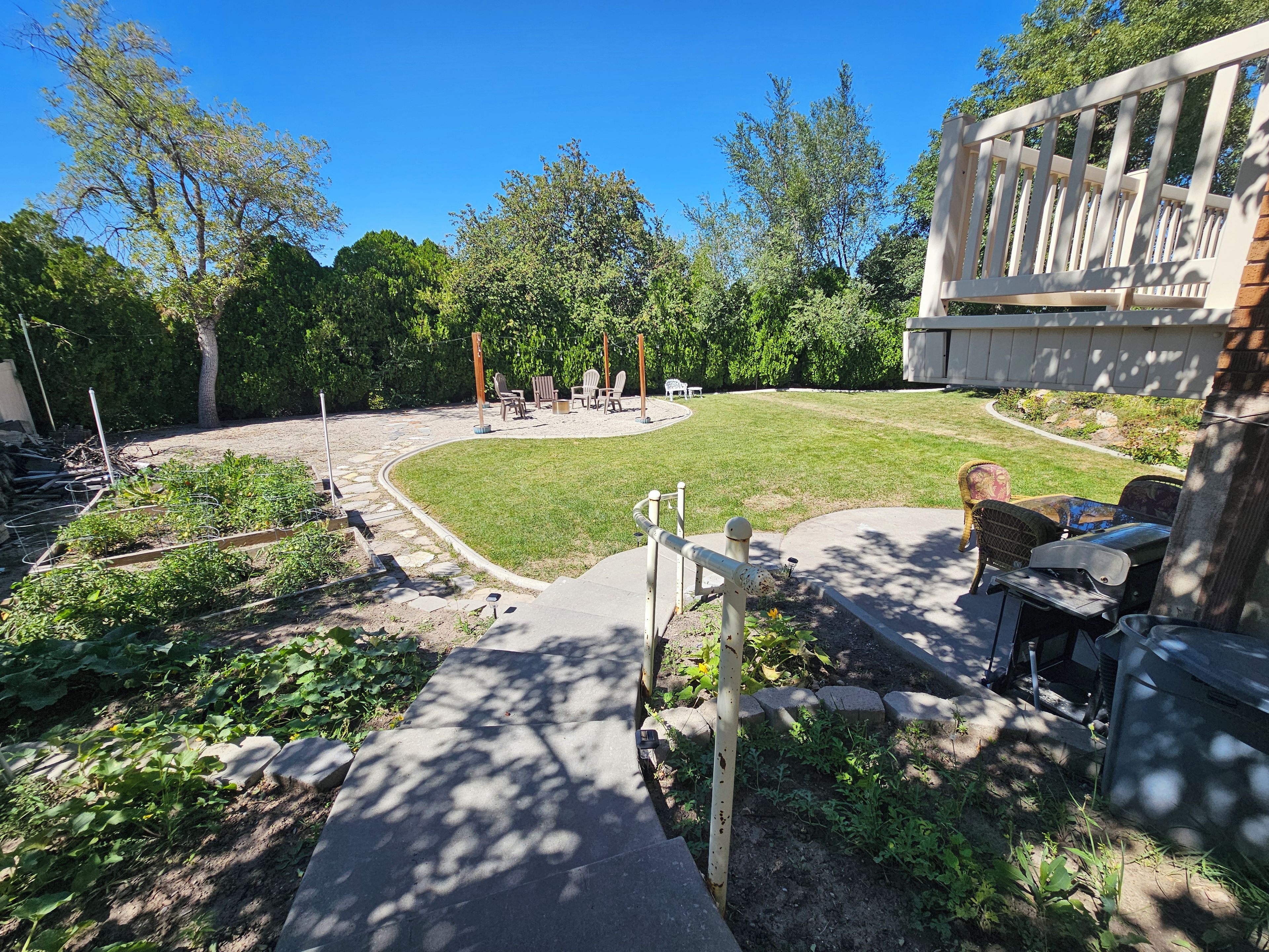 Ein Garten mit Rasenfläche, Blumenbeeten, Gartenmöbeln und einer Terrassenanlage.