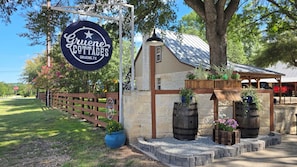 A sign for Gruene Cottages with a rustic building, wooden barrels, and potted plants. - Rosemary Gruene Cottage Studio (New Braunfels)