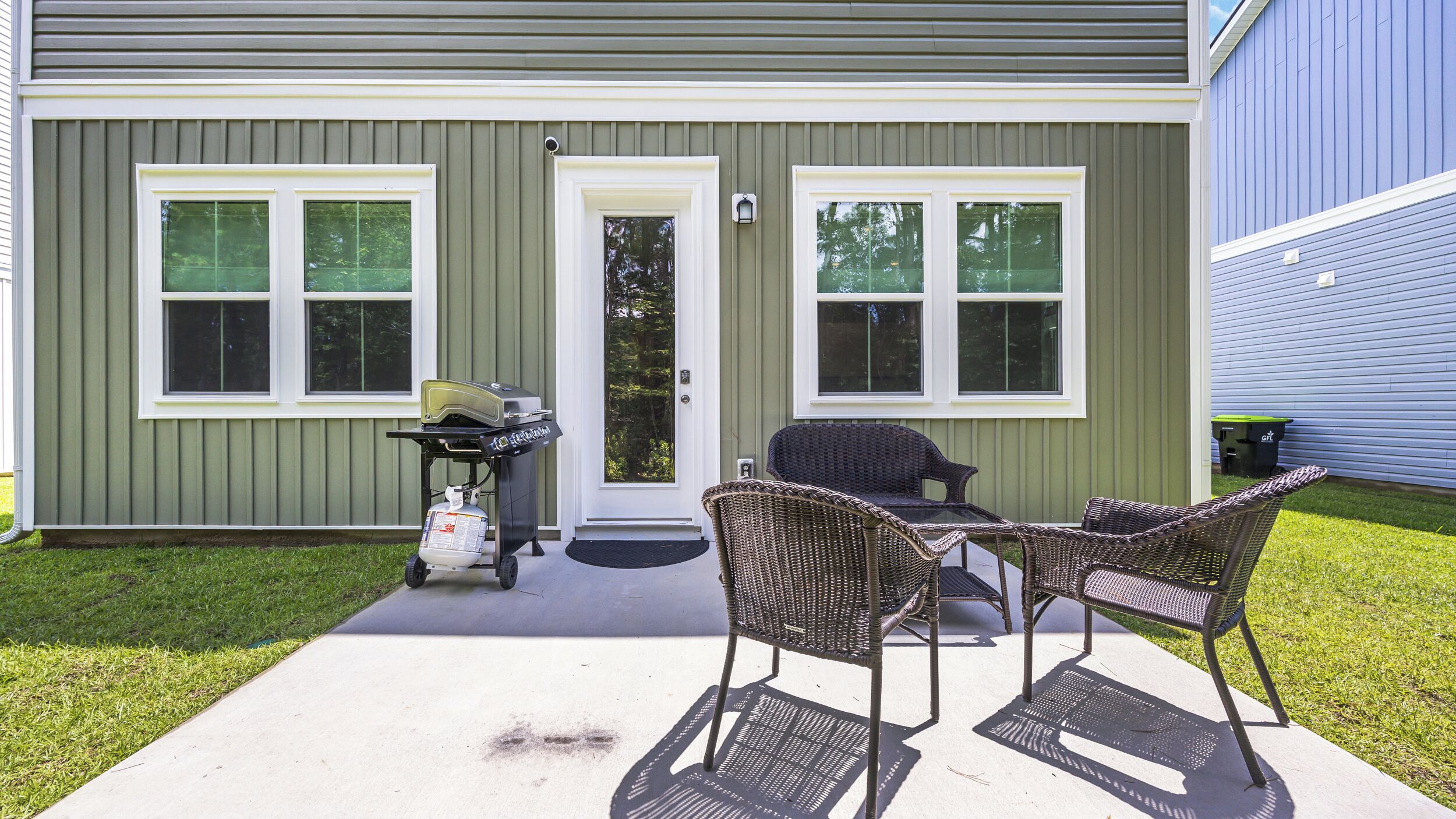 Ein Wohngebäude mit überdachter Terrasse, Gartenmöbeln und einem Grill.