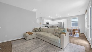 A modern living room with a sectional sofa, a dining area with a table and chairs, and a kitchen with white cabinets and appliances. - Enjoyable 4-bedroom house with AC in charming Little River (Little River)