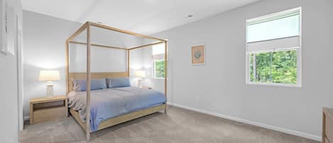 Un dormitorio con cama con dosel, dos mesitas de noche, un ventanal con vistas a la vegetación y una obra de arte colgada en la pared.