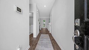 A hallway with a wooden floor, white walls, and a door with a keypad lock. - Enjoyable 4-bedroom house with AC in charming Little River (Little River)