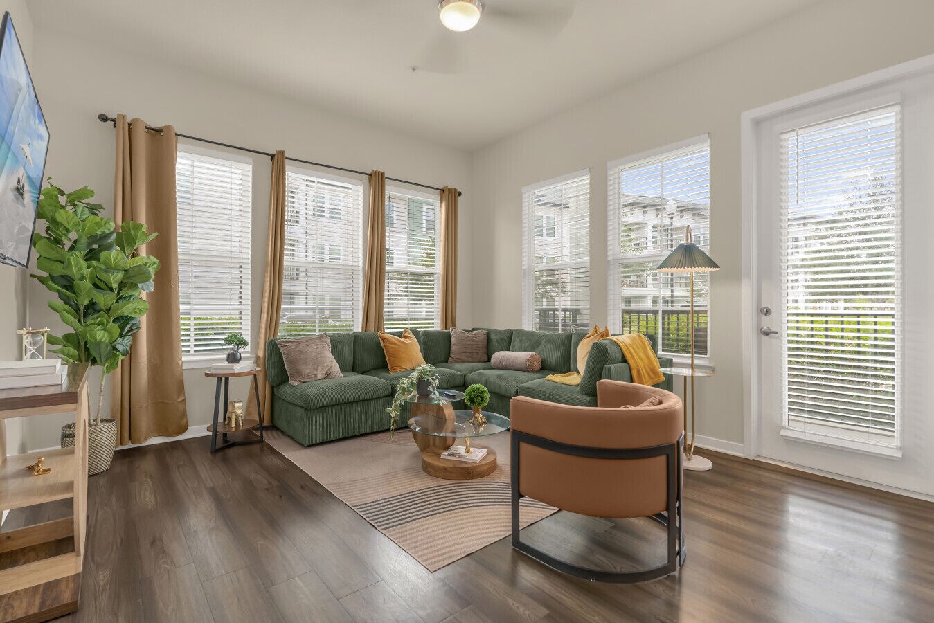 A spacious living room with a green sofa set, a wooden coffee table, and a large window with blinds.