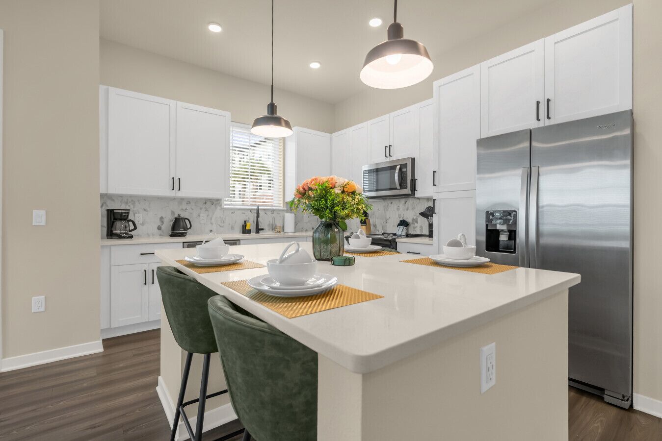 A modern kitchen with white cabinets, a stainless steel refrigerator, and a central island with seating.