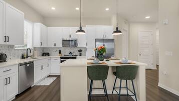 A modern kitchen with white cabinets, stainless steel appliances, and a central island with bar stools.