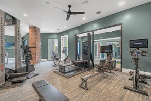 Ein Fitnessraum mit Trainingsgeräten, einem großen Spiegel und einem Deckenventilator.